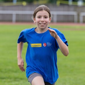 A picture of a young person taking part in a Team Bath Tribe summer holiday athletics camp in Bath Building Society t-shirts, August 2024
