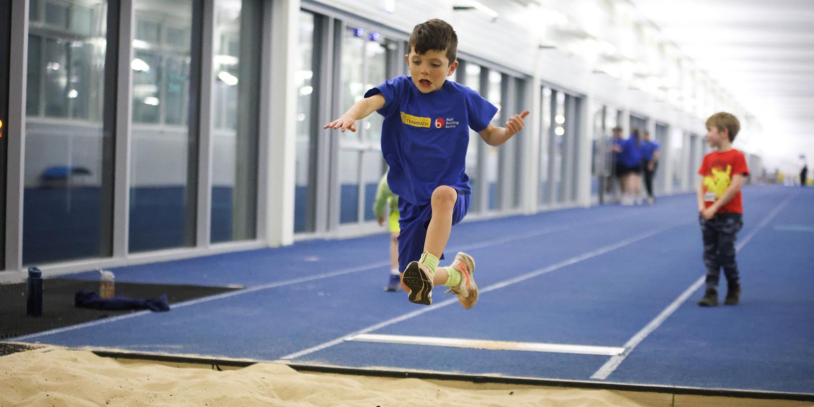 A picture of a boy jumping into an indoor sand pit during a Team Bath Tribe after-school athletics session.