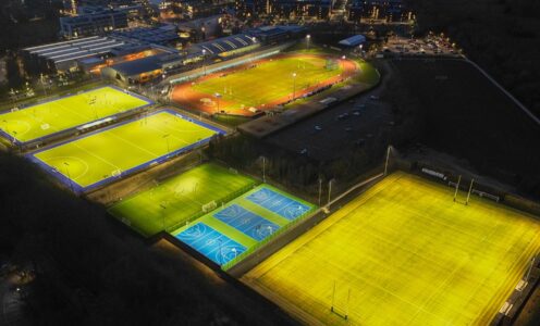 An aerial shot of the floodlit hockey pitches, 400m athletics track, infield, 3G pitches, muliti-use games area (MUGA) and Sports Training Village with the University campus and city of Bath on the horizon.