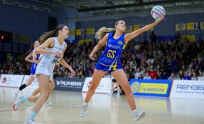 A photo of Team Bath Netball goal-shooter Katherine Mansfield controlling the ball at full stretch in front of a stand full of spectators during the 54-47 NXT Gen League victory over Birmingham Panthers in April 2025.