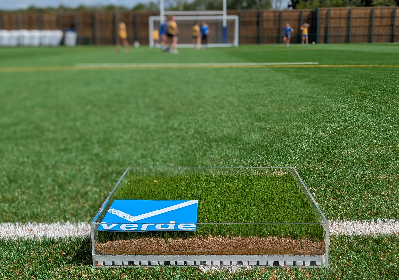 A photo of a cross-section of the fully-recyclable 3G pitch at the University of Bath in a glass box, showing the various layers from shockpad at the bottom to artificial turf at the top. It is placed on top of the actual 3G pitch.