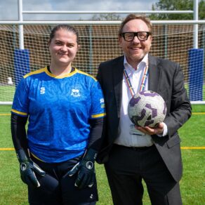 A photo of Professor Phil Taylor, Vice-Chancellor and President of the University of Bath, with women's football 1st XI goalkeeper Susie English at the official opening of a new 3G pitch. Professor Taylor is holding a football.
