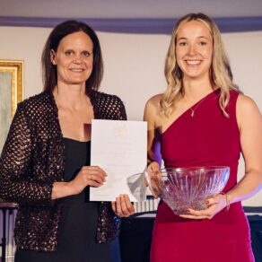 A photo of Professor Cassie Wilson presenting a certificate to Sports Personality of the Year Charlotte Gregory, who is also holding a glass bowl, at the 2025 Blues Awards for University of Bath students