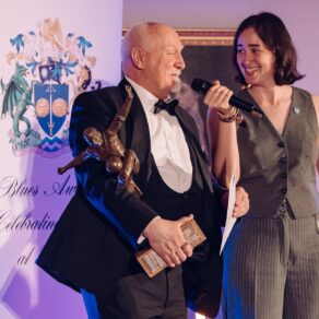 A photo of University of Bath Swimming Club coach Andrei Vorontsov speaking into a microphone during an on-stage interview at the 2025 Blues Awards