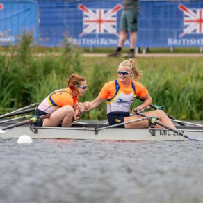 Bath University Boat Club rowers Beatrice Hughes and Ella Fullman in their boat on the river, smiling and congratulating each other after winning Championship Women’s Double Sculls gold at the 2025 British Rowing Club Championships.