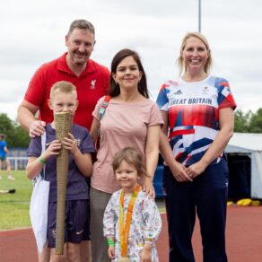 A photo of Paralympic swimming champion Stephanie Millward, right, standing with a family of mum, dad and two children - they are all looking at the camera and the son is holding an Olympic Torch.