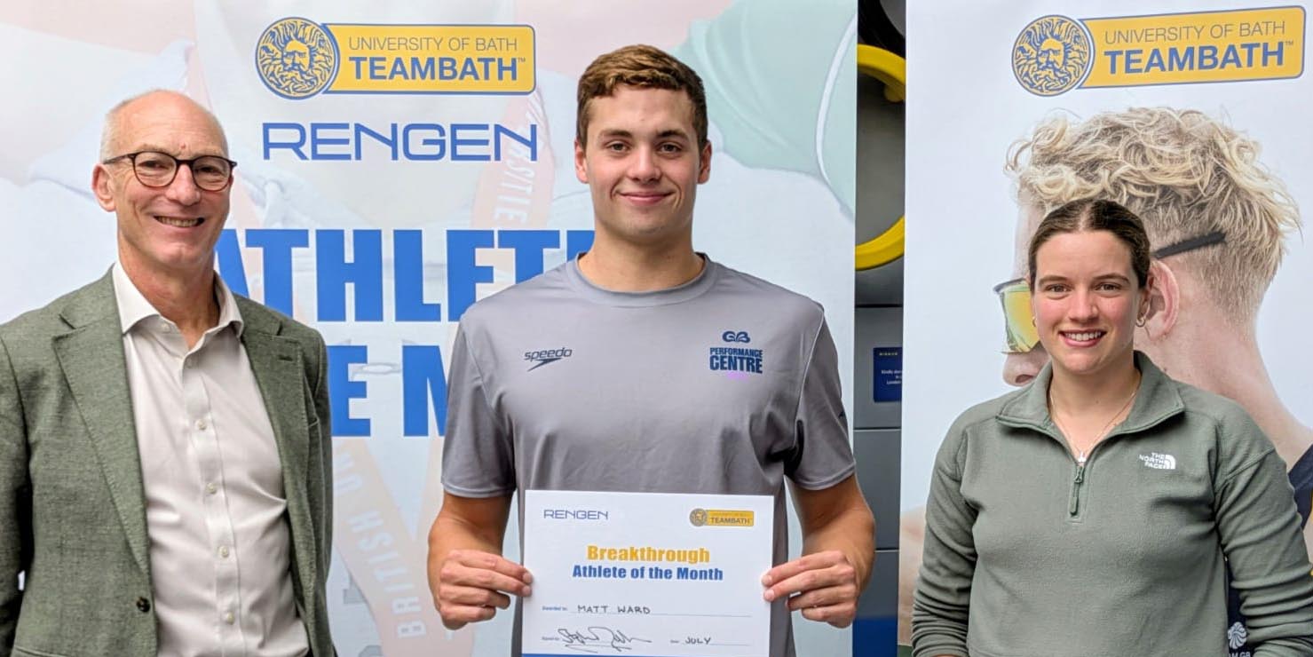 Aquatics GB swimmer Matthew Ward, the Team Bath Rengen Athlete of the Month for July 2025, flanked by University of Bath Director of Sport Stephen Baddeley (left) and Performance Sport Officer Sarah Collin. He is holding a certificate and the trio are standing in front of a board saying Athlete of the Month.