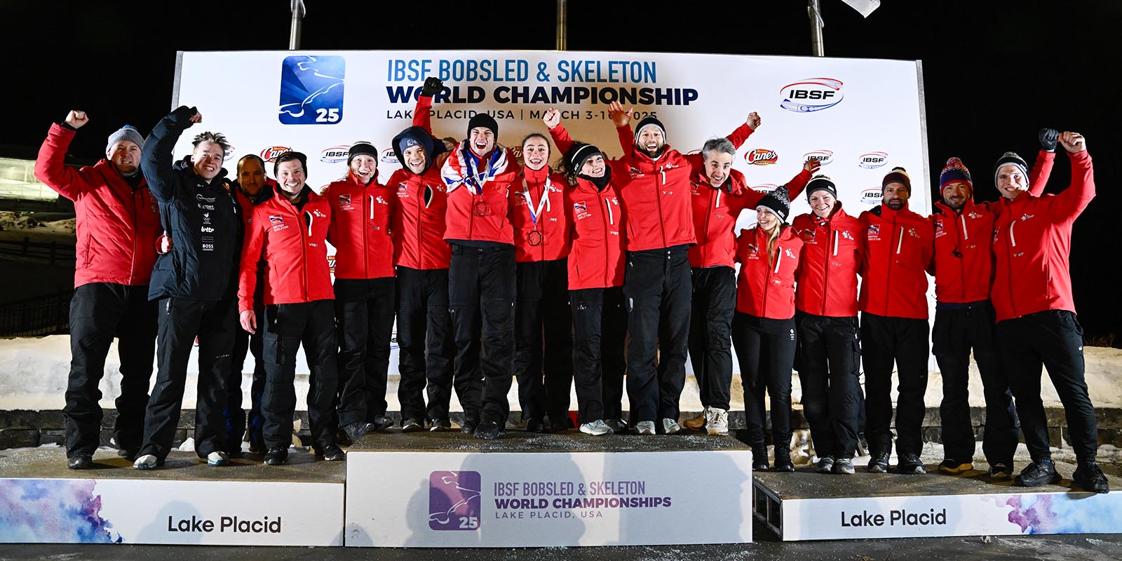 A group picture of British Skeleton athletes, coaches and support staff standing on the podium at the 2025 IBSF World Championships.