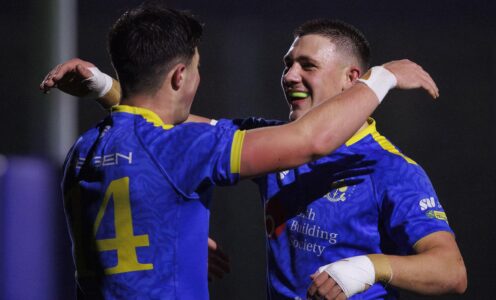 Two rugby players wearing blue kit go to hug in celebration after scoring a try.