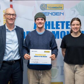 Ross Telfer, wearing a hat and holding a certificate, standing of front of an Athlete of the Month board. Standing either side of her are Stephen Baddeley, University of Bath Director of Sport, and Sarah Collin, Performance Sport Officer. 
