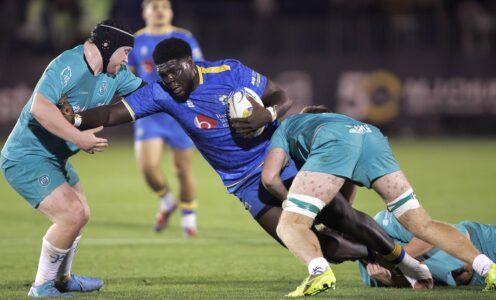 University of Bath rugby player Enoch Opoku-Gyamfi, wearing blue, being tackled by two Exeter players, wearing green.