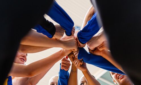 A Team Bath Netball hands-in huddle, as seen from below looking up.