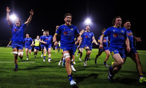 University of Bath Rugby Club players, wearing blue, run towards the camera in celebration after a crucial win against Loughborough