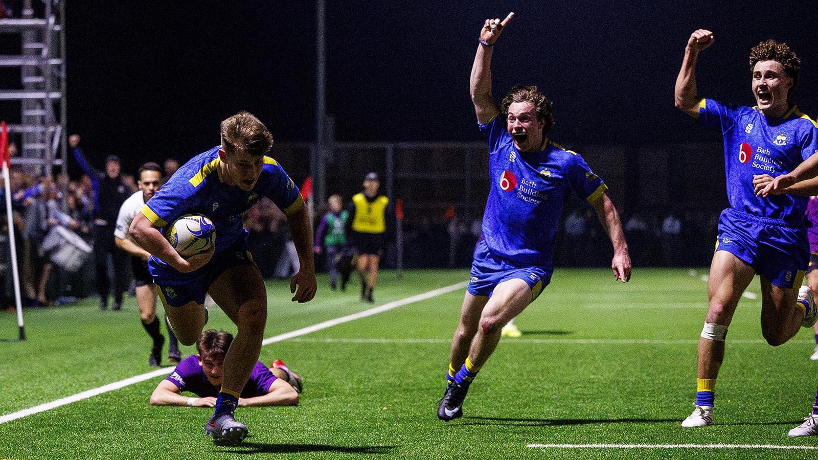 Two players raise their arms in celebration as team-mate Harry Walker prepares to dive across the line for a Bath try