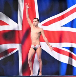Artistic swimmer Ranjuo Tomblin stands in front of a Union Flag at the start of a routine.