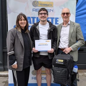 (From left) Rengen's Sarah Baker, swimmer Christian Ryan and University of Bath Director of Sport Stephen Baddeley standing in front of an Athlete of the Month pop-up banner. Christian is holding a certificate and Stephen is holding a Built for Athletes backpack.