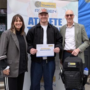 (From left) Rengen's Sarah Baker, rugby player Max Pearce and University of Bath Director of Sport Stephen Baddeley standing in front of an Athlete of the Month pop-up banner. Max is holding a certificate and Stephen is holding a Built for Athletes backpack.