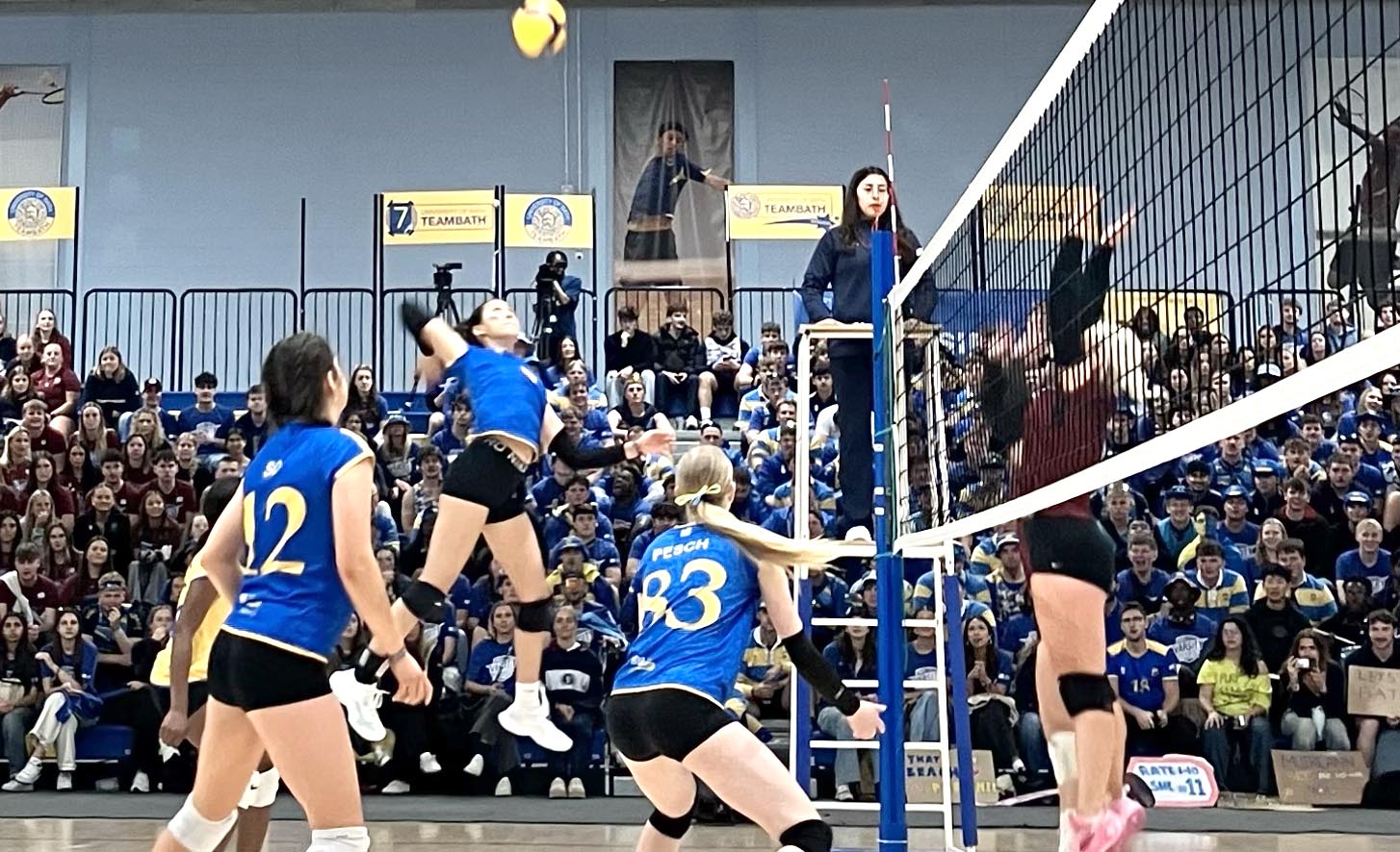 A University of Bath volleyball player leaps to spike a ball as a crowd of spectators watches on
