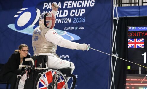 British Para Fencer Dimitri Coutya, wearing full kit and visor, punches the air after landing a hit. Behind him is a sign saying "Para Fencing World Cup, Bradenton 2026"