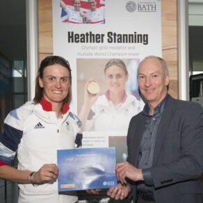 Heather Stanning is presented with a framed Hall of Fame certificate by University of Bath Director of Sport Stephen Baddeley. They are stood in front of Heather's Hall of Fame panel.