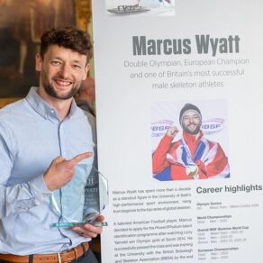 Marcus Wyatt, holding a glass trophy, standing in front of a Hall of Fame panel featuring his name, photo and career achievements