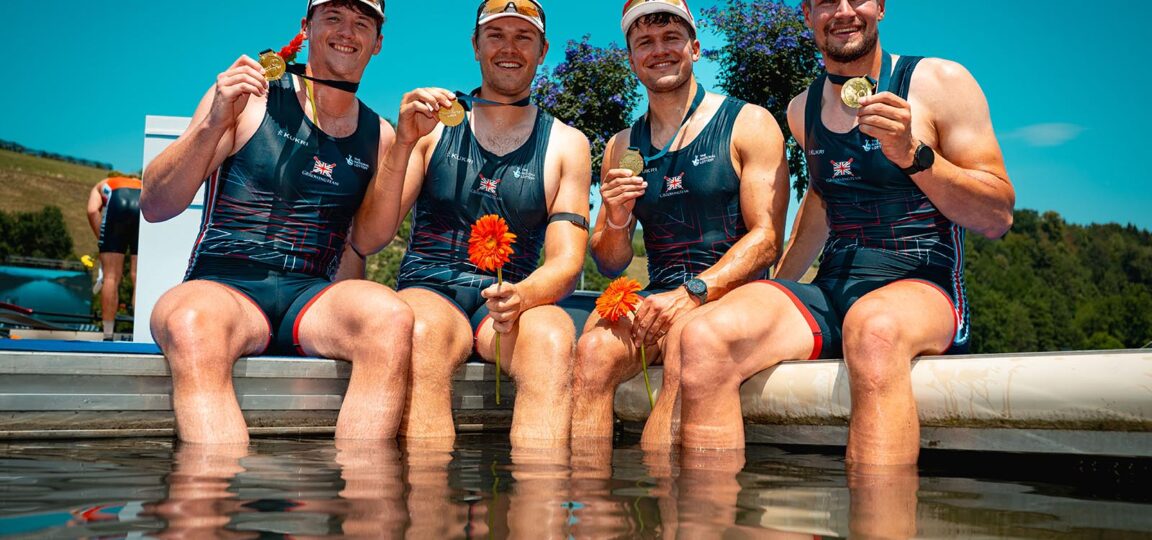 The four members of the GB Rowing Team men's quad, sitting with their feet in water while holding gold medals.
