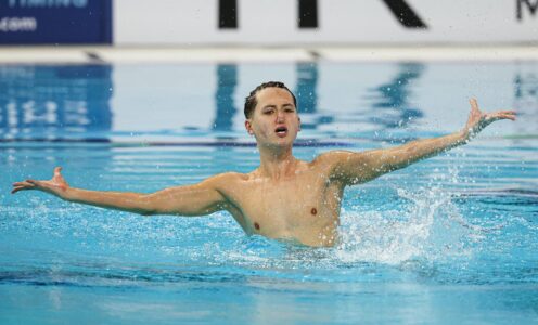 Artistic swimmer Ranjuo Tombin in the swimming pool during a free routine, his arms are outstretched.