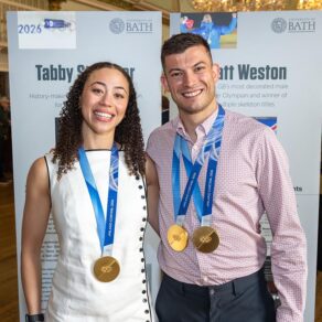 Skeleton Olympic Champions Tabby Stoecker and Matt Weston smiling at the camera with their gold medals around their necks.