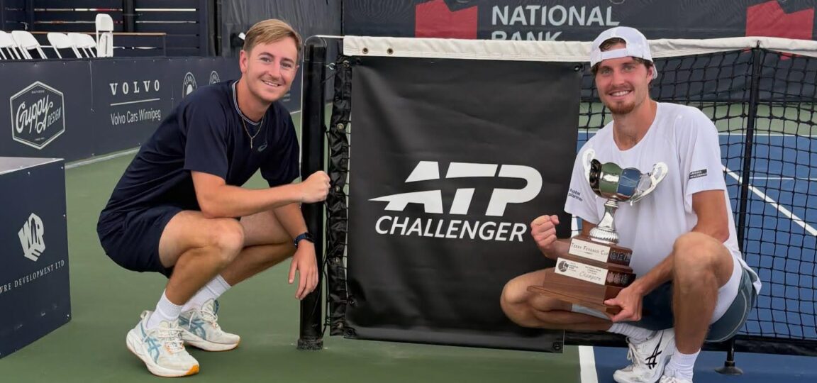 Coach Tiarnan Brady (left) and tennis player Toby Samuel kneeling next to a tennis net featuring the ATP Challenger Tour logo. Toby is holding a trophy.