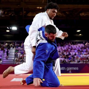 Two judoka, one wearing white and the other in blue, grappling on a mat as a crowd watches on
