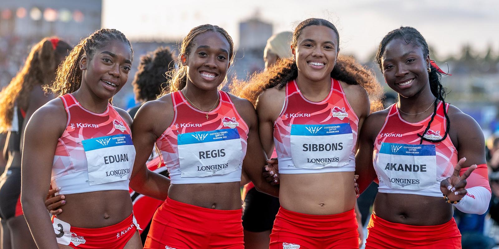 Four athletes, wearing red, smiling at the camera