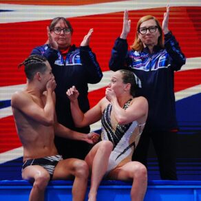 Ranjuo Thorpe and Izzy Thorpe, sitting, cover their mouths in disbelief as two coaches applaud behind them