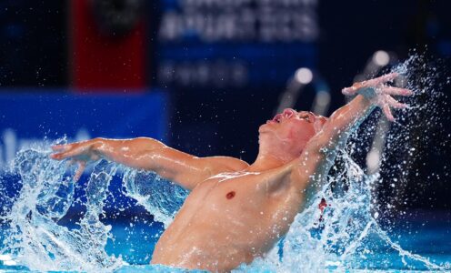 Water splashing around Ranjuo Tomblin's outstretched arms as he performs an artistic swimming routine