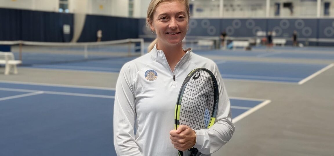 Alicia Barnett, Performance Tennis Coach, on the indoor tennis courts at Team Bath. She is holding a racquet.