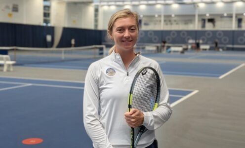 Alicia Barnett, Performance Tennis Coach, on the indoor tennis courts at Team Bath. She is holding a racquet.