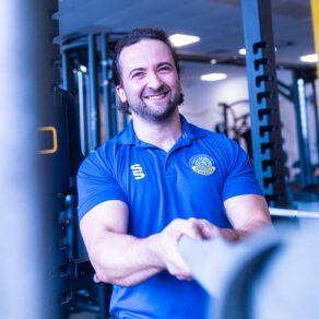 An instructor in a blue Team Bath t-shirt in a gym environment