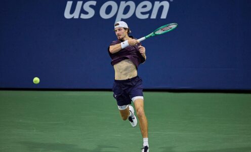 Toby Samuel hitting a forehand on a green tennis court with a blue backdrop behind him featuring the US Open logo
