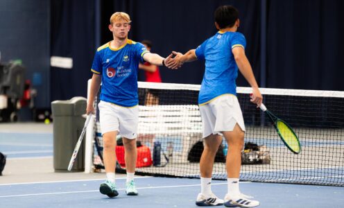 Two tennis players, wearing blue, slap palms on an indoor court