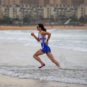 GB rower Emma Nicholson sprinting out of the sea onto a beach during a race